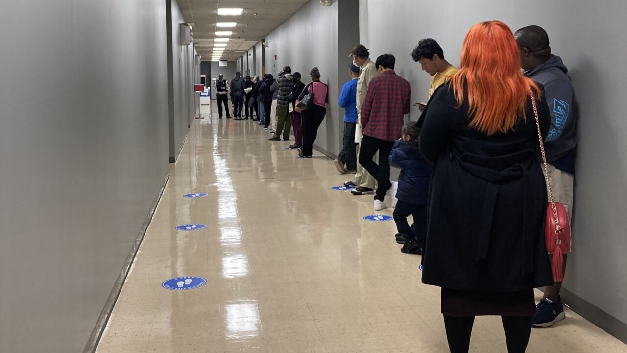 People standing in line down long gray hallway.